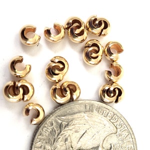May include: A close-up of 14 gold-colored metal bead caps, some are open and some are closed. The bead caps are arranged in a circle around a US quarter.