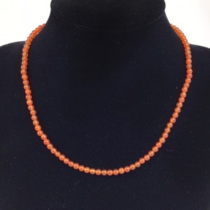 May include: A necklace made of small, round, orange carnelian beads.