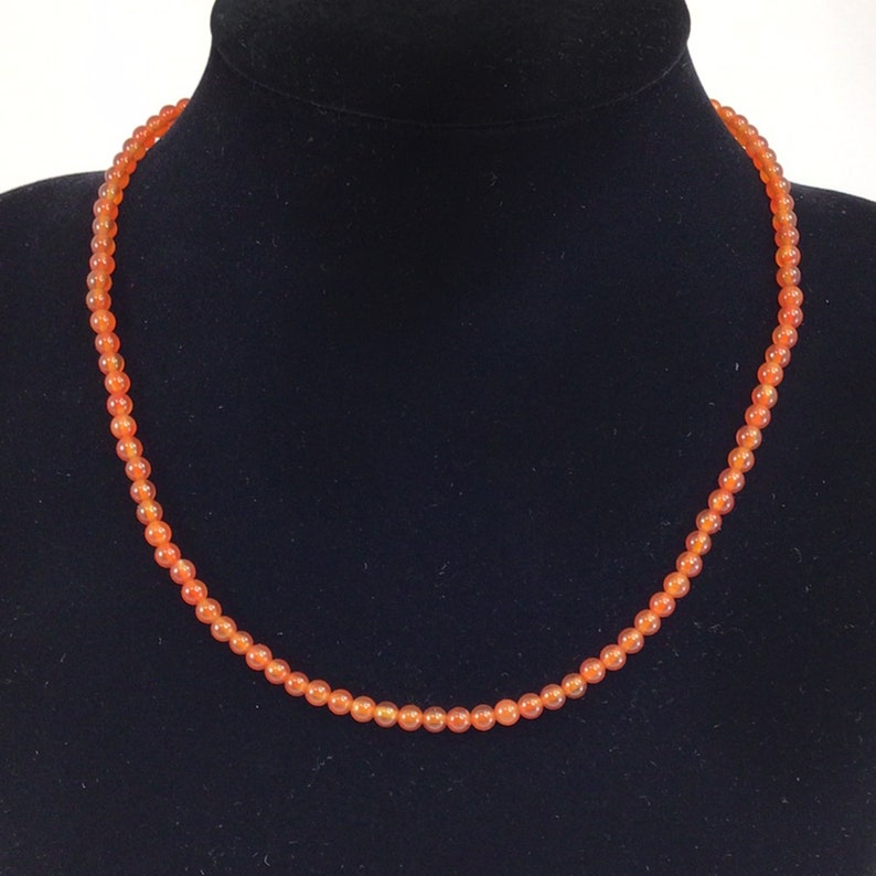 May include: A necklace made of small, round, orange carnelian beads.