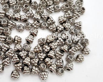 May include: A collection of small, metallic silver-toned beads with a textured, bumpy surface. Each bead features a central hole for threading. The beads are scattered across the frame, displaying a shiny, reflective finish and a uniform shape.