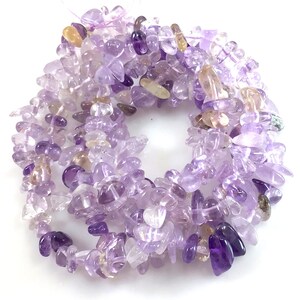 May include: A strand of amethyst chip beads in shades of purple and lavender. The beads are irregular in shape and size, with some having a more pointed or elongated shape.