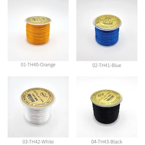 May include: Four spools of elastic beading cord in orange, blue, white, and black. Each spool has a gold label with Japanese text. The spools are labeled 01-TH40-Orange, 02-TH41-Blue, 03-TH42-White, and 04-TH43-Black.