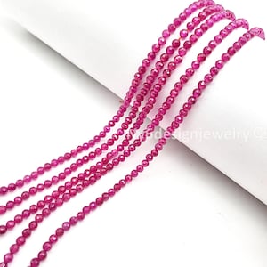 May include: Strands of faceted, small, round, ruby-colored beads. The beads are strung together, creating a delicate and elegant appearance. The beads are a vibrant shade of pinkish-red, perfect for jewelry making or crafting.