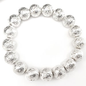 May include: A silver bracelet featuring large, textured beads. The beads have a rough, pitted surface, giving them a unique, organic appearance. The bracelet is circular and sits against a white background, highlighting the metallic sheen of the beads.