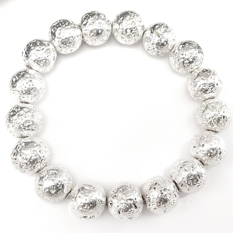 May include: A silver bracelet featuring large, textured beads. The beads have a rough, pitted surface, giving them a unique, organic appearance. The bracelet is circular and sits against a white background, highlighting the metallic sheen of the beads.