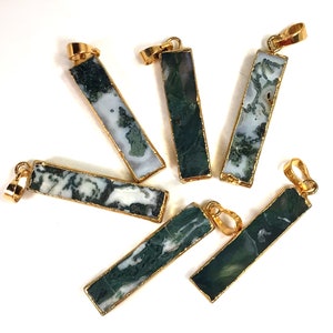 May include: Rectangular moss agate pendants with gold-colored metal trim and bails. The pendants feature a mix of white and green patterns. The gold-colored metal has a smooth, shiny finish. The pendants are displayed against a white background.
