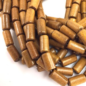 May include: Close-up of a collection of cylindrical wooden beads in various shades of brown. The beads are strung together, showcasing their smooth, polished texture and natural wood grain. Ideal for jewelry making or craft projects.