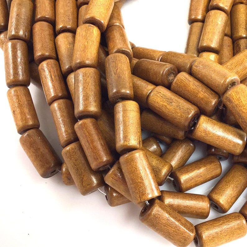 May include: Close-up of a collection of cylindrical wooden beads in various shades of brown. The beads are strung together, showcasing their smooth, polished texture and natural wood grain. Ideal for jewelry making or craft projects.