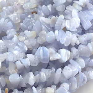May include: Close-up of a collection of light blue and white gemstone chips. The chips are irregularly shaped and appear to be polished. The gemstones are scattered, creating a textured surface.