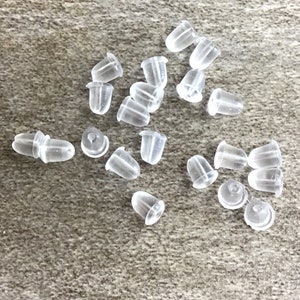 May include: A group of clear plastic earring backs scattered on a light brown surface.