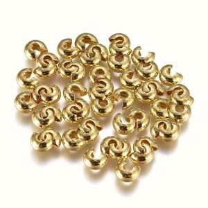May include: A pile of gold-colored metal crimp beads. The beads are small and round, with a hole in the center. They are used to secure jewelry findings.
