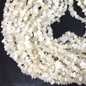 May include: A strand of white moonstone chip beads. The beads are irregular in shape and have a slightly translucent appearance.