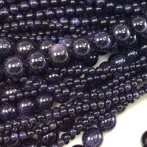 May include: A close-up of a pile of dark blue gemstone beads. The beads are round and have a sparkly, glittery finish.