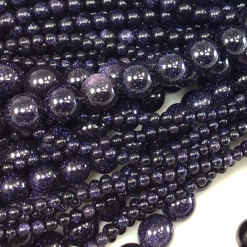 May include: A close-up of a pile of dark blue gemstone beads. The beads are round and have a sparkly, glittery finish.