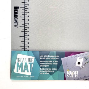 May include: A gray, non-slip, laser-printed beading mat with the text "TREASURE MAT" and "12.5in x 9.25 in (31.75 x 23.5 cm)". The mat is made of natural rubber and is designed for beading and jewelry making.