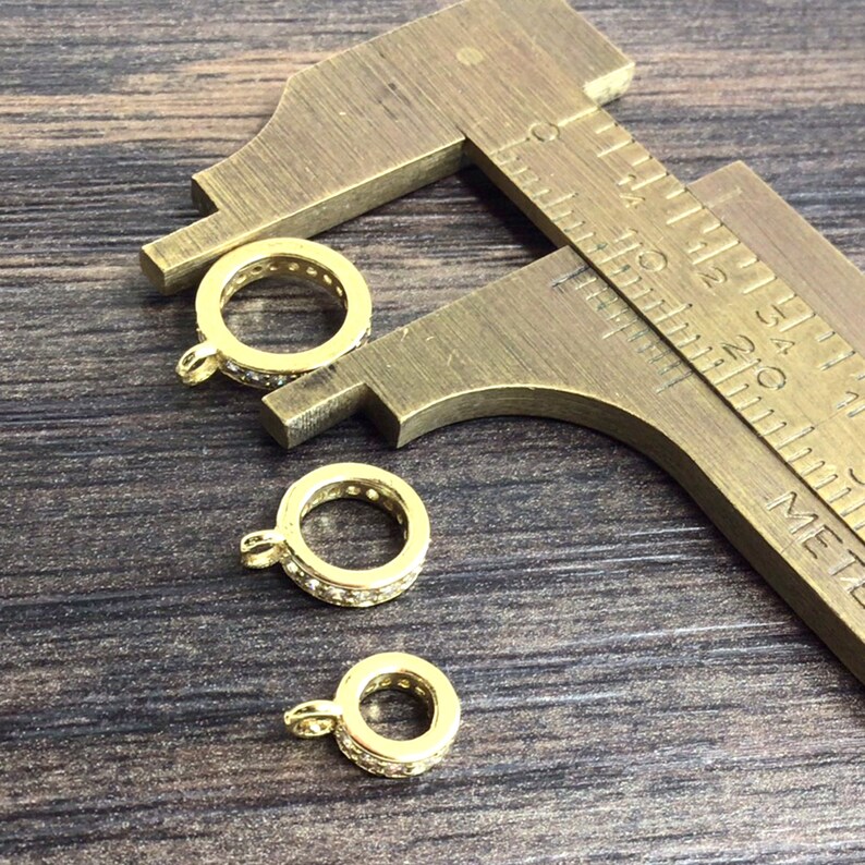 K&ouml;nnte beinhalten: Drei goldfarbene Metallringe mit klaren Kristallverzierungen. Die Ringe werden mit einer Schieblehre gemessen.