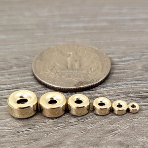 Pu&ograve; includere: Quattro anelli di metallo color oro di diverse dimensioni. Gli anelli sono rotondi e hanno una finitura liscia e lucida. Gli anelli sono disposti in ordine di dimensione, con l'anello pi&ugrave; grande a sinistra e l'anello pi&ugrave; piccolo a destra.