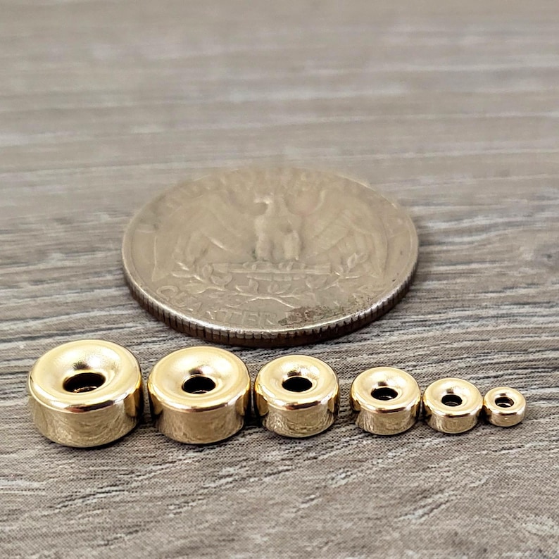 Pu&ograve; includere: Quattro anelli di metallo color oro di diverse dimensioni. Gli anelli sono rotondi e hanno una finitura liscia e lucida. Gli anelli sono disposti in ordine di dimensione, con l'anello pi&ugrave; grande a sinistra e l'anello pi&ugrave; piccolo a destra.