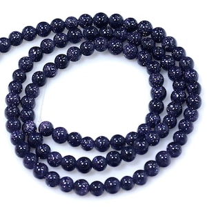 May include: A strand of dark blue gemstone beads with a speckled, starry appearance. The beads are round and smooth, and they are strung on a clear thread.