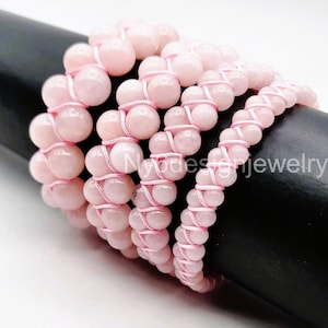 May include: A set of five pink gemstone bracelets with pink string. Each bracelet is made with round beads and a criss-cross pattern.