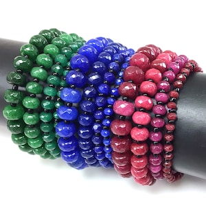 May include: A set of five bracelets made with faceted gemstone beads. The bracelets are in shades of green, blue, and pink. The beads are strung on black thread.