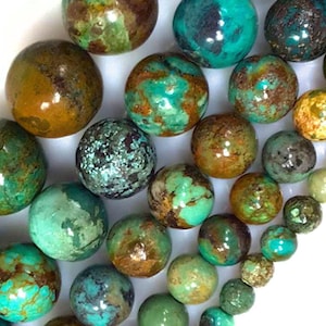 May include: A collection of polished, round gemstones in various sizes and colors. The stones feature a mix of turquoise, brown, and green hues, with unique patterns and textures. Some stones have a mottled appearance, while others are a solid color.
