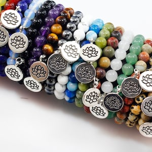 May include: A stack of colorful beaded bracelets with silver lotus flower charms. The bracelets are made with various gemstones, including amethyst, tiger's eye, and green aventurine.