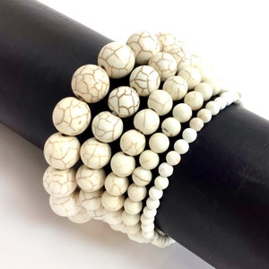 May include: A stack of white howlite bead bracelets with varying sizes and textures. The beads have a natural, slightly rough finish and are arranged in a graduated pattern.