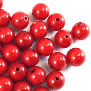 May include: A group of bright red round beads with a hole in the center. The beads are made of plastic and have a glossy finish.