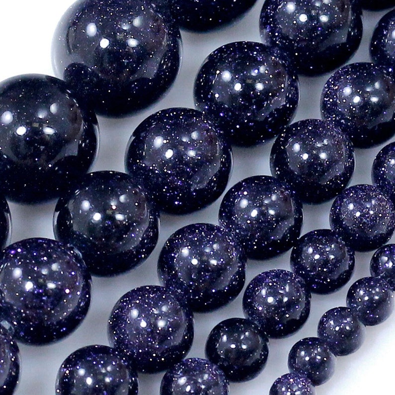 May include: A strand of dark blue gemstone beads with a speckled, starry appearance. The beads are round and smooth, and they are arranged in a line.
