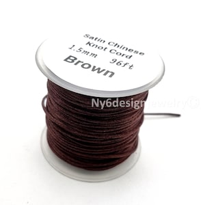 May include: A spool of brown satin Chinese knot cord with a white label reading Satin Chinese Knot Cord, 1.5mm, 96ft, Brown. The cord is wrapped around a clear plastic spool, and the text Ny6designjewelry is visible on the side of the spool.