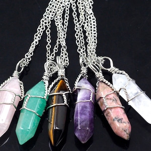 May include: Six silver chain necklaces with wire-wrapped crystal pendants. The crystals are in various colors, including pink, green, brown, purple, and pink and white.