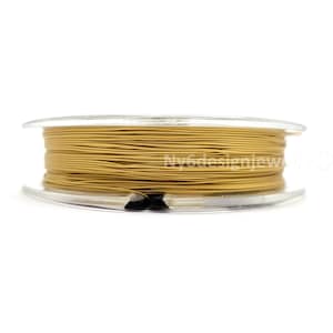 May include: A spool of gold-colored beading wire. The wire is tightly wound on a clear plastic spool. The spool is set against a white background. The wire appears to be made of a flexible material.
