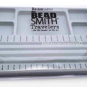 May include: A gray plastic beading tray with multiple compartments and a ruler marked in inches. The tray has the text "BEAD SMITH Travelers" printed on it. The tray is designed for beading and jewelry making.