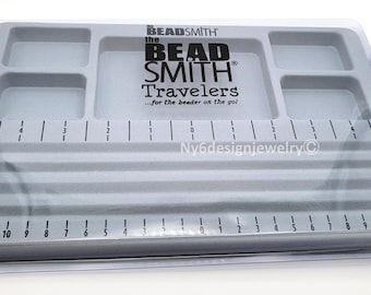 May include: A gray plastic beading tray with multiple compartments and a ruler marked in inches. The tray has the text "BEAD SMITH Travelers" printed on it. The tray is designed for beading and jewelry making.