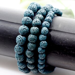 May include: Four stacked bracelets made of dark blue lava rock beads. Each bracelet is made of round beads with a rough, textured surface.