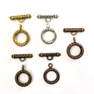 May include: A collection of seven metal toggle clasps for jewelry making, featuring various metallic finishes including gold, silver, copper, and bronze. Each set consists of a circular ring and a matching bar, all decorated with intricate patterns.
