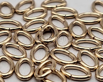 May include: A pile of gold-colored oval jump rings. The rings are small and have a smooth, polished finish.