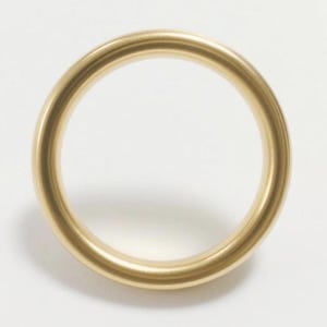 May include: A gold-colored metal ring, circular in shape, with a smooth, polished surface. The ring is set against a white background, highlighting its form and color. The ring's design is simple and elegant.