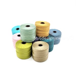 May include: A collection of colorful spools of waxed cord in various shades, including teal, pink, green, yellow, and blue. The spools are arranged in a cluster, showcasing the different colors and textures of the cord. Ideal for crafting and jewelry making.