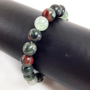May include: A green, red, and black gemstone bracelet with round beads. The bracelet is on a black surface.