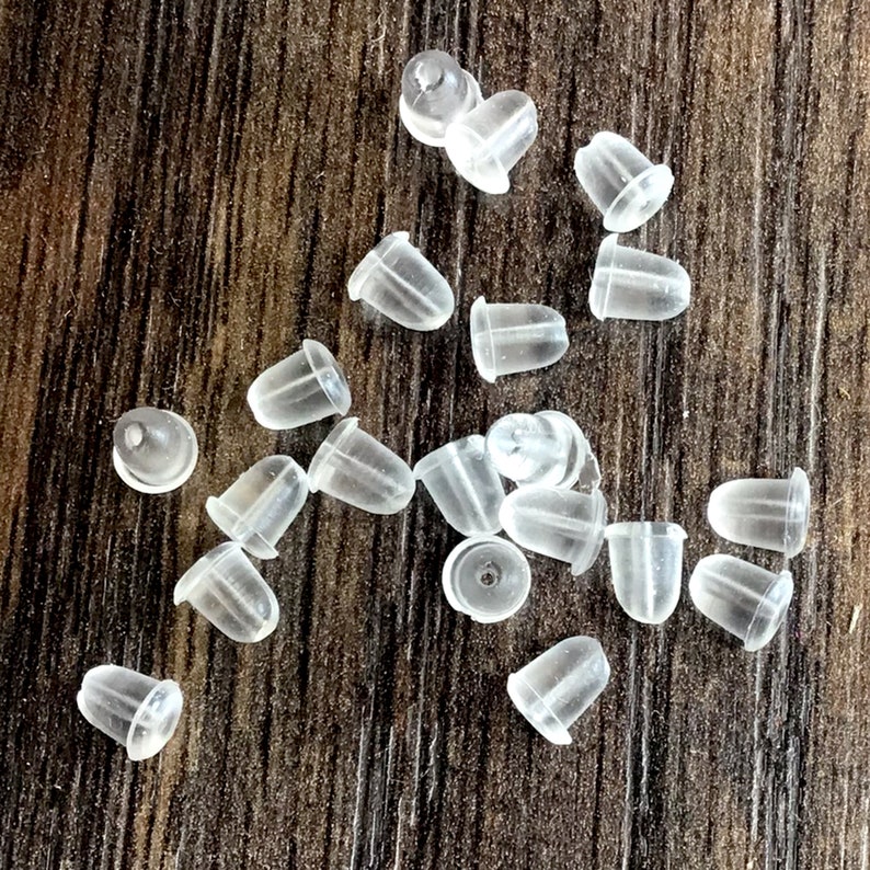 May include: A group of clear plastic earring backs scattered on a wooden surface.