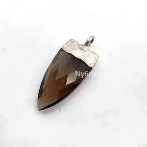 May include: A faceted, brown gemstone pendant with a silver-colored metal cap and loop. The pendant has a pointed, elongated shape. The text "Ny6designjewelry ©" is visible on the side of the pendant.