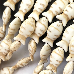 May include: A strand of white ceramic fish beads with brown stripes. The beads are strung on a clear string and are all facing the same direction.