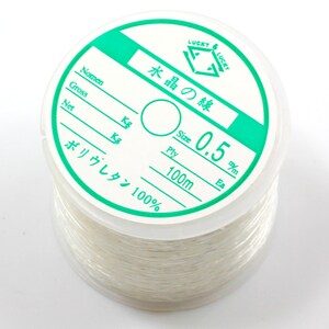 May include: A spool of white elastic cord labeled "Lucky Lucky" with the text "Water Crystal Line" in Japanese. The spool is labeled with the size "0.5 mm", "100m", and "Polyurethane 100%".