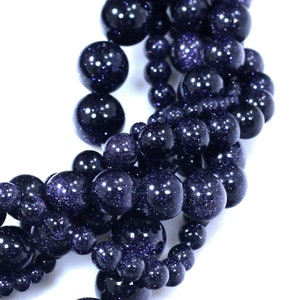May include: A strand of dark blue gemstone beads with a speckled, glittery finish. The beads are round and have a smooth, polished surface.
