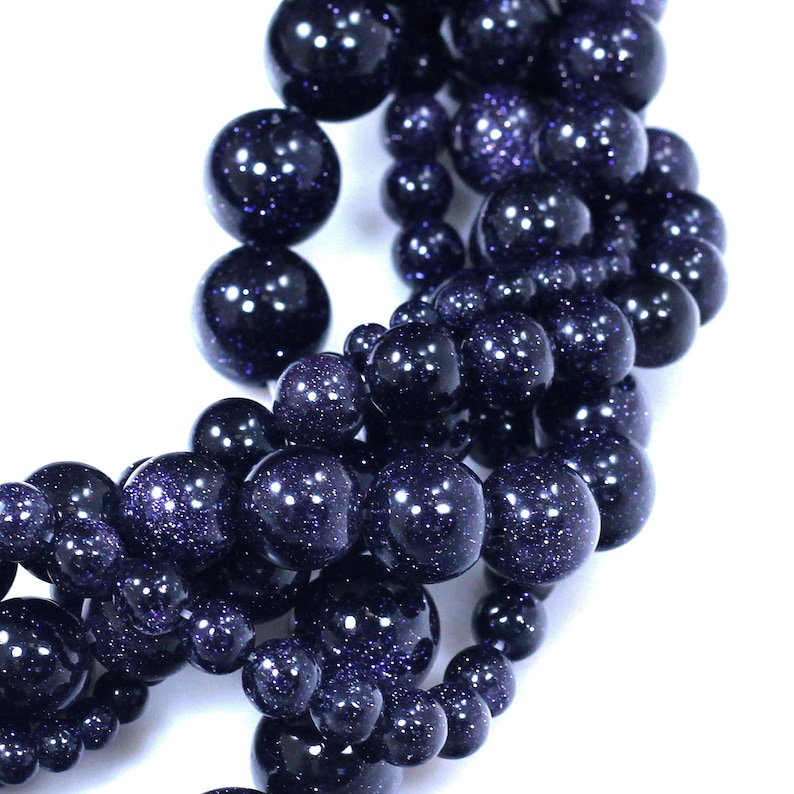 May include: A strand of dark blue gemstone beads with a speckled, glittery finish. The beads are round and have a smooth, polished surface.