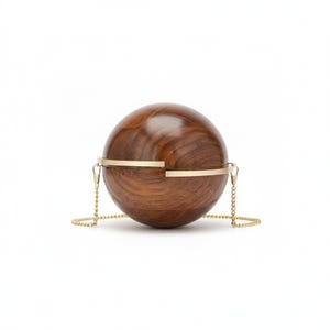 Puede incluir: Un bolso de mano esférico de madera con un acabado marrón oscuro. El bolso está adornado con bandas metálicas doradas y una delicada correa de cadena. El diseño es minimalista y elegante, adecuado para diversas ocasiones.