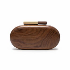 May include: A dark brown wooden clutch bag with an oval shape. The bag has a visible wood grain pattern and a gold-coloured metal clasp. It features a small, dark brown wooden handle.