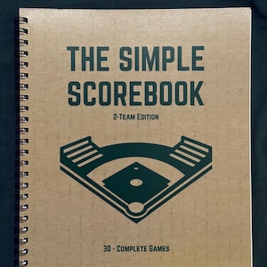 May include: A spiral-bound baseball scoreboard with a kraft paper cover. The cover features the text "THE SIMPLE SCOREBOOK" in dark green, along with a baseball field graphic and the text "2-TEAM EDITION" and "30 - COMPLETE GAMES".